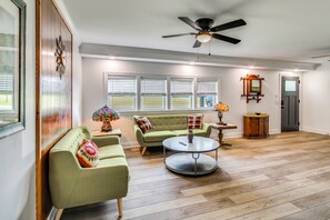 Ein geräumiges Wohnzimmer mit einem grünen Sofa, einem runden Couchtisch und einem Deckenventilator.