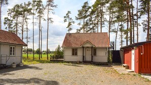 En lille, etetagers bygning med røde tegltag, omgivet af høje træer og en grusvej.