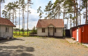 A small, single-story building with a red-tiled roof, surrounded by tall trees and a gravel driveway. - Gorgeous home in Gärds Köpinge with WiFi (Gärds Köpinge)