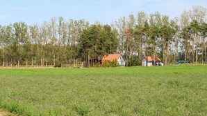 Et landligt landskab med et marker, træer og et lille hus med rødt tag.