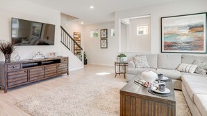 Ein modernes Wohnzimmer mit einer Holz-Unterhaltungsecke, einem großen Flachbildfernseher, einem grauen Sofa und einem Couchtisch mit Dekorationselementen.