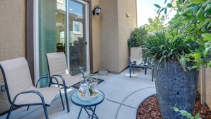 Eine Terrasse mit Tisch und Stühlen, ein großer Kübelpflanztopf und eine Glastür, die in einen Innenraum führt.