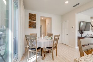 A dining area with a round table, four chairs, and a view of a living room with a TV and a plant. - New Build w/ Patio! Roseville Extended Stay (Roseville)