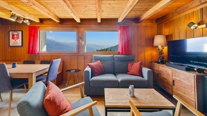 Een knus interieur van een blokhut met houten wanden, een bank, een televisie en een eethoek.