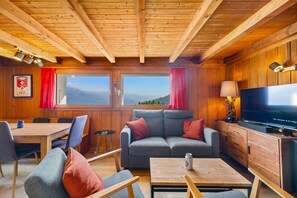 Ein gemütliches Blockhaus-Interieur mit Holzwänden, einer Couch, einem Fernseher und einem Essbereich.