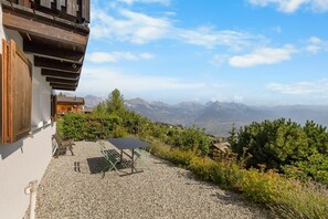 Eine Terrasse mit Tisch und Stühlen, ein Holzzaun und Blick auf Berge.