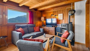 Een gezellig interieur van een blokhut met een bank, stoelen, een televisie en een houtkachel.
