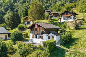 Un ensemble de chalets en bois, entourés d’une végétation luxuriante, dont un chalet plus imposant se distingue par son balcon et un drapeau suisse.