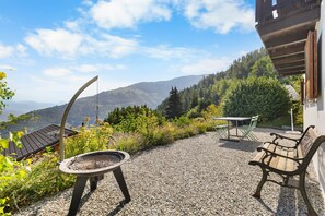 Une terrasse avec une table et deux bancs, entourée de gravier et de verdure, offrant une vue sur un paysage montagneux.