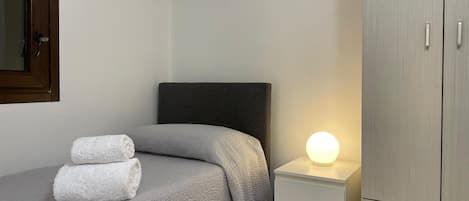 A bedroom with a bed, a nightstand with a lamp, and a wardrobe.