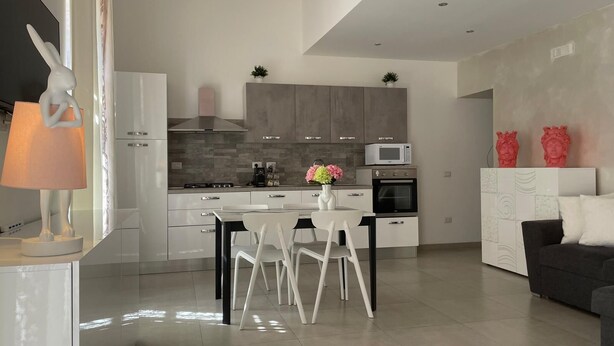 A modern kitchen with a dining area, white cabinetry, and a grey sofa. - Arricriati near Ortigia by Wonderful Italy (Siracusa)