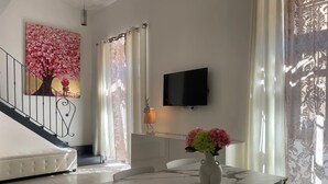 A dining area with a marble table, white chairs, a vase with flowers, a painting of a tree, and a TV on the wall. - Arricriati near Ortigia by Wonderful Italy (Siracusa)