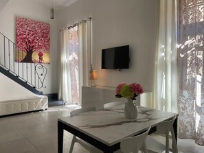 A dining area with a marble table, white chairs, a vase with flowers, a painting of a tree, and a TV on the wall. - Arricriati near Ortigia by Wonderful Italy (Siracusa)