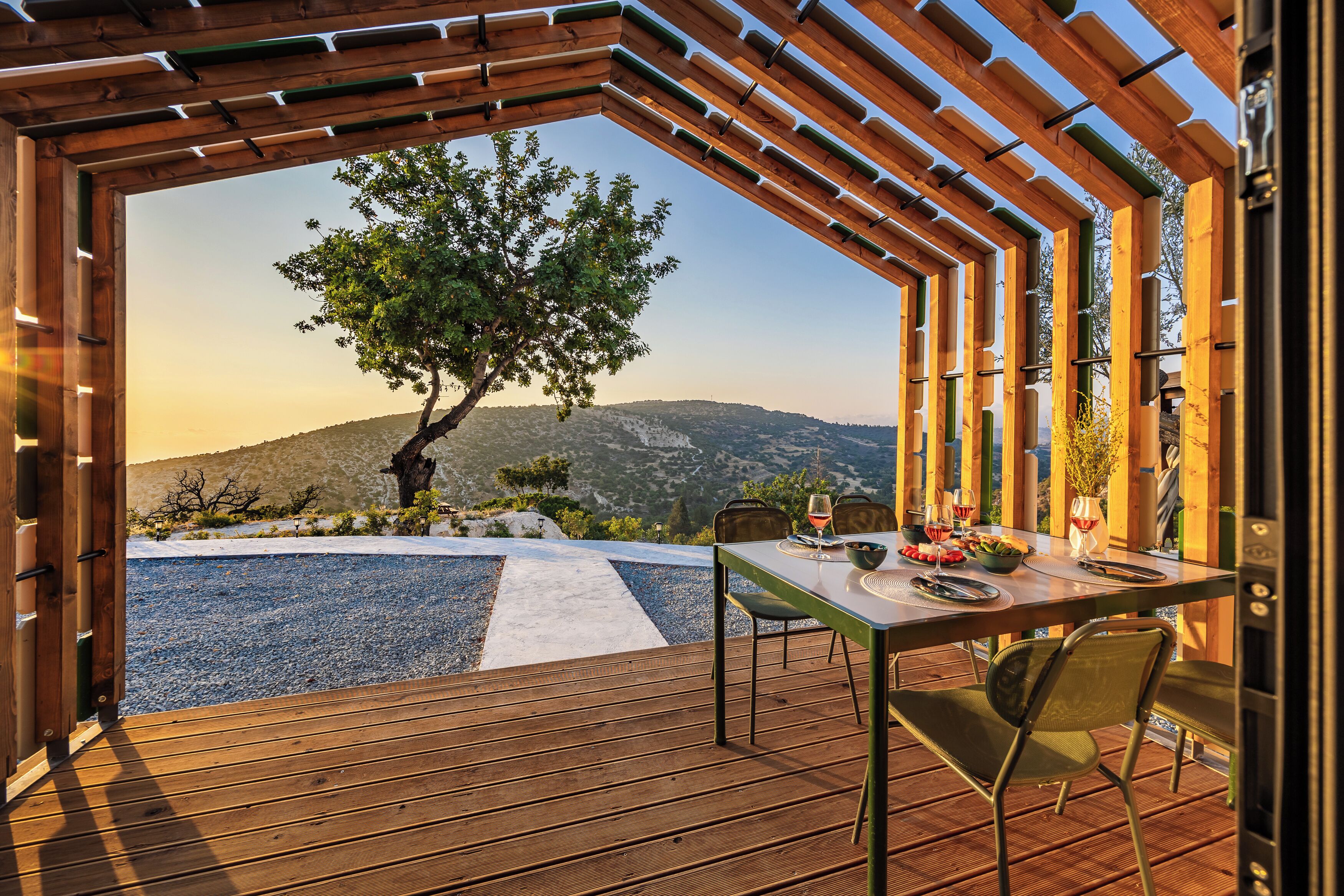 An outdoor dining area with a table and chairs, a view of a tree and mountains, and a pergola structure.