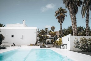 A modern white building with a swimming pool, surrounded by palm trees and other vegetation. - Villa Amonita – Luxury Villa, Heated Pool & Private Garden (Tiagua)