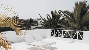 Una terrazza panoramica con due poltrone bianche e un tavolino, circondata da palme e un parapetto bianco.