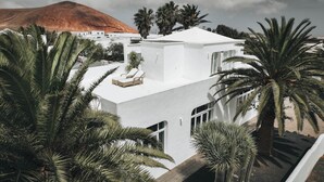 Un bâtiment moderne, de couleur blanche, doté d’un toit plat, entouré de palmiers et avec une montagne en arrière-plan.