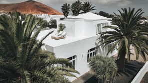 A modern white building with a flat roof, surrounded by palm trees and a mountain in the background. - Villa Amonita – Luxury Villa, Heated Pool & Private Garden (Tiagua)