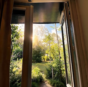 An open door leading to a garden with a path, surrounded by greenery and trees.