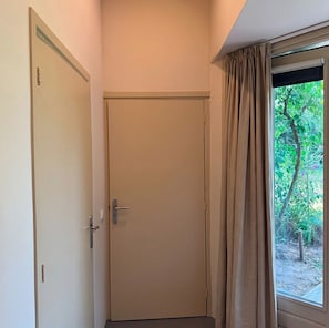 A closed door with a handle, a window with curtains, and a view of greenery outside.