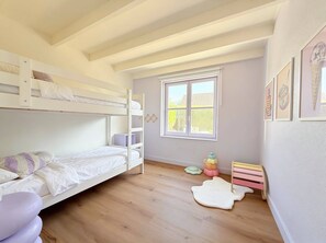 Ein Kinderzimmer mit Etagenbetten, einem Fenster und einer kleinen Spielecke.