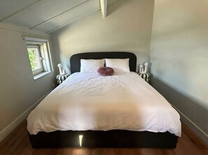 A neatly made bed with white linens and a single decorative pillow in a room with a sloped ceiling and a small window. - The Sea, Plopsaland & France | Fisherman's Cottage in De Panne (De Panne)