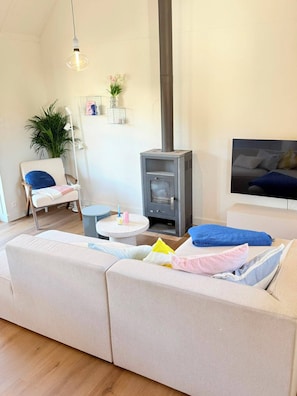 A cozy living room with a sofa, a small table, a TV, and a wood-burning stove. - The Sea, Plopsaland & France | Fisherman's Cottage in De Panne (De Panne)