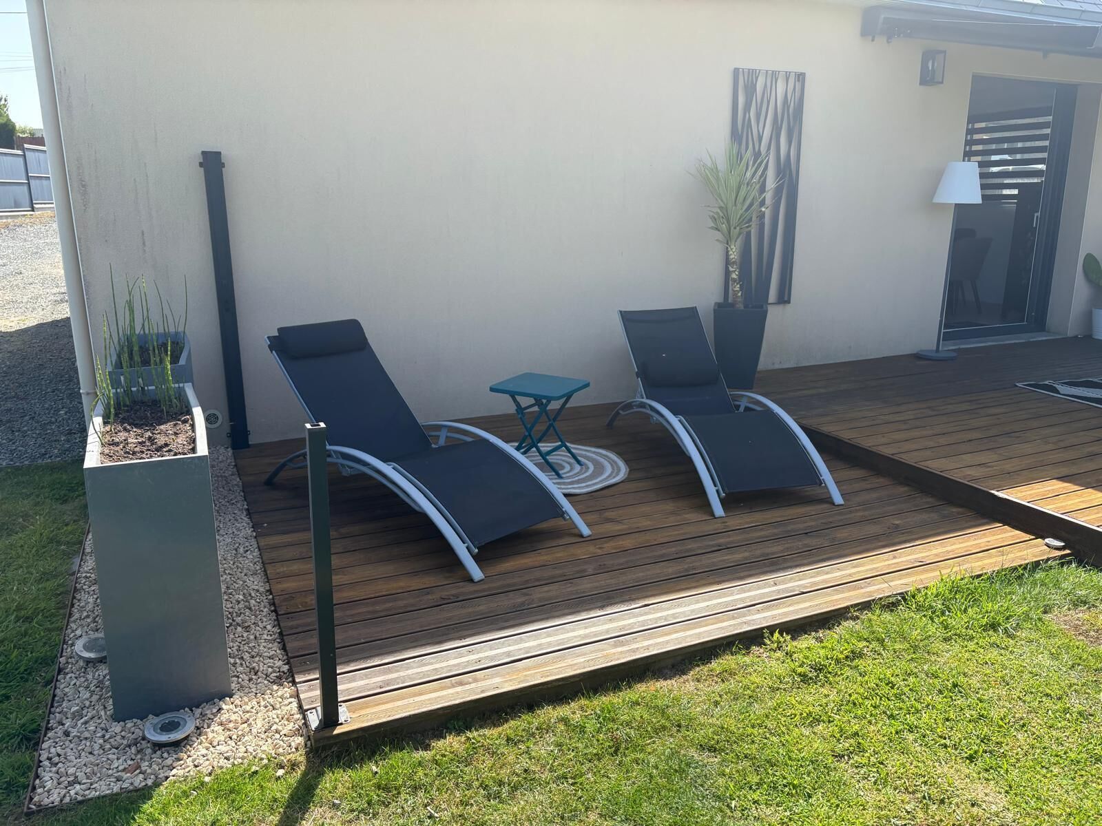 Eine Terrasse mit zwei Liegestühlen und einem kleinen Tisch, umgeben von einer niedrigen Mauer und einem Blumentopf.
