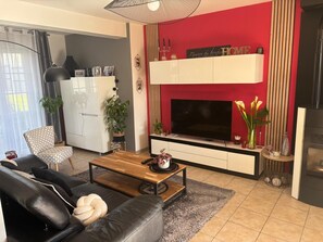 Ein modernes Wohnzimmer mit Flachbildfernseher, einer Couch, einem Couchtisch und einer roten Akzentwand.