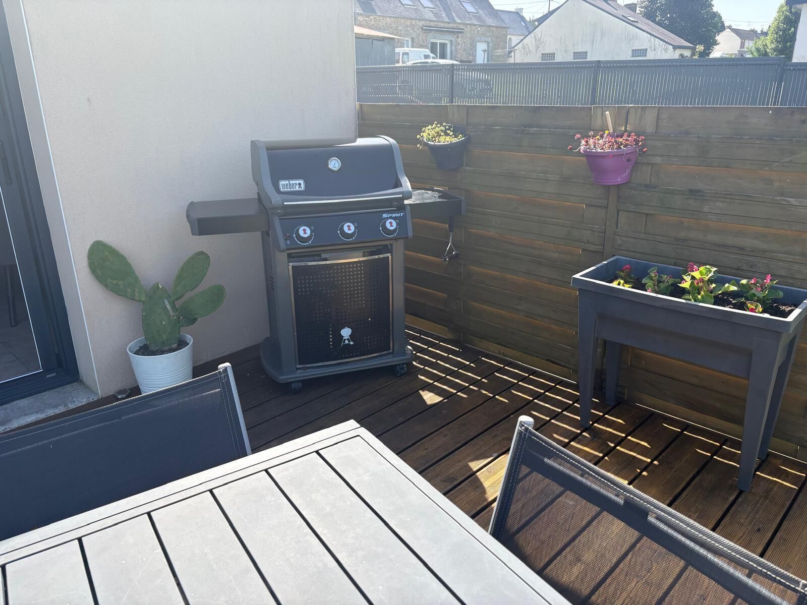 Une terrasse avec un barbecue, une table, des chaises et des plantes en pot.