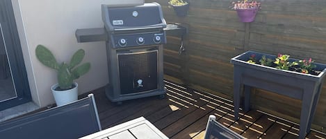 Une terrasse avec un barbecue, une table, des chaises et des plantes en pot.