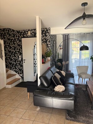 Ein modernes Wohnzimmer mit einem schwarzen Ledersofa, einer Treppe und einem Essbereich mit einem gemusterten Sessel.