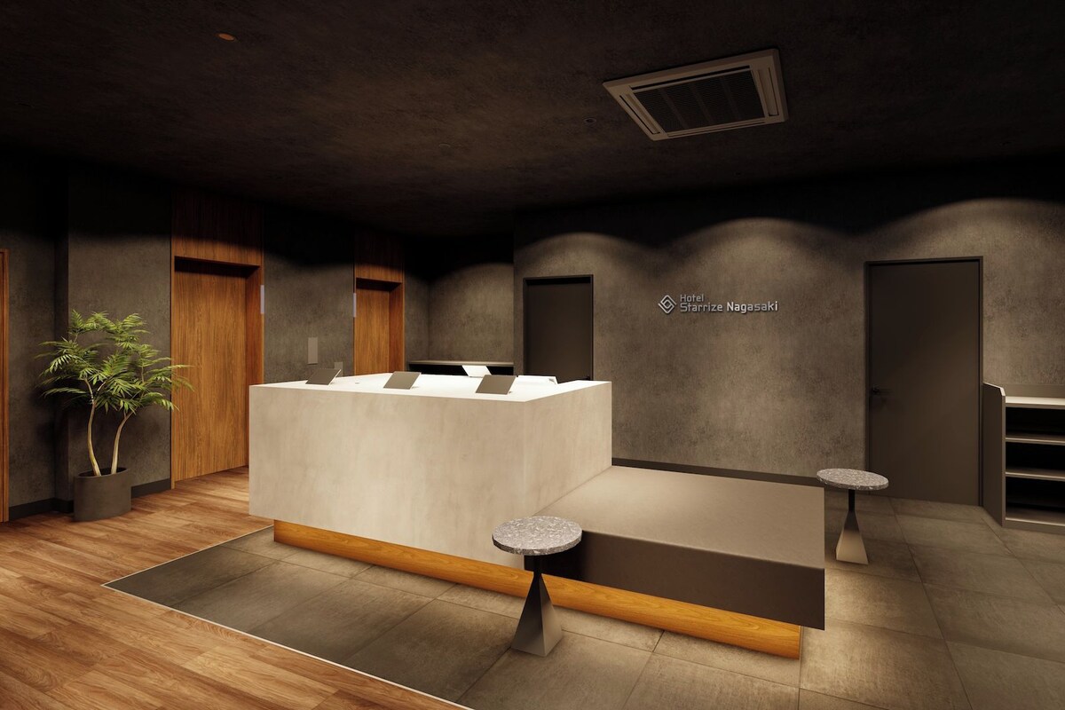 A hotel reception area with a reception desk, a potted plant, and a view of the sky through a window.