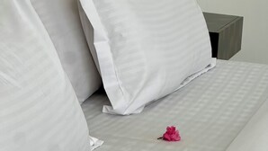 A neatly made bed with white linens and pillows, a wooden headboard, and a small bedside table with a green object on it.