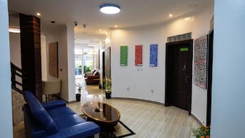 Un hall de hotel con distribución curva, una recepción, una zona de estar con sillas azules y una mesa de centro.