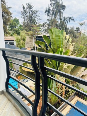 Ein Balkon mit Metallgeländer, der Blick auf einen Swimmingpool und üppiges Grün freigibt.