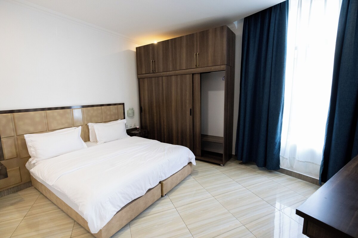 Ein Hotelzimmer mit Bett, Kleiderschrank, Nachttisch und einem Fenster mit Vorhängen.