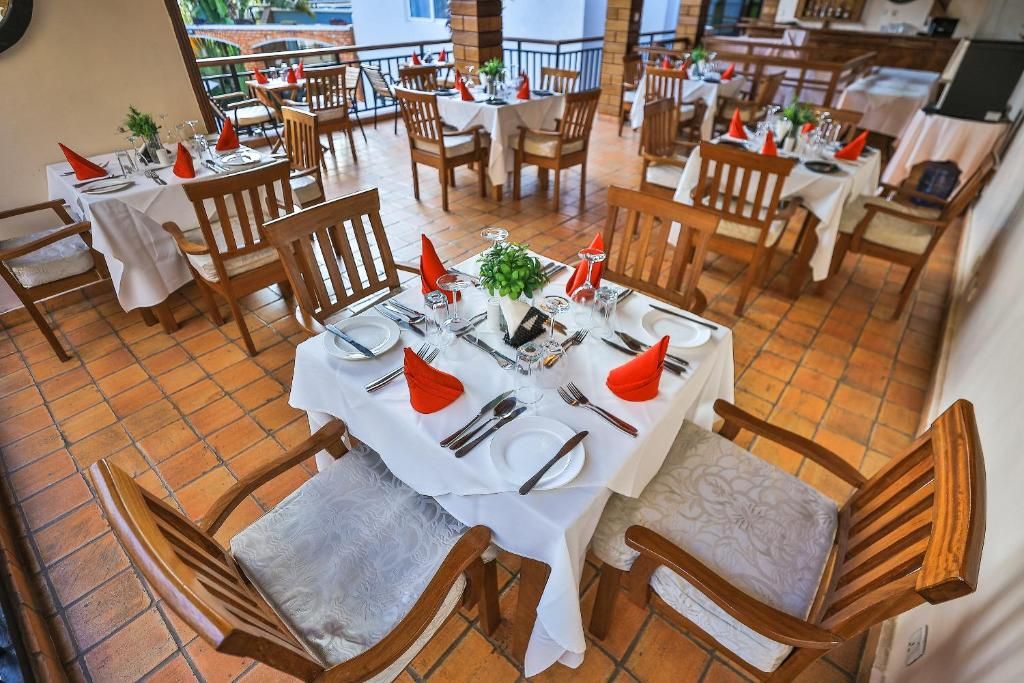A restaurant with multiple tables set for dining, each with chairs, white tablecloths, and red napkins.