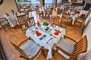 Ein Restaurant mit mehreren gedeckten Tischen, jeweils mit Stühlen, weißen Tischdecken und roten Servietten.