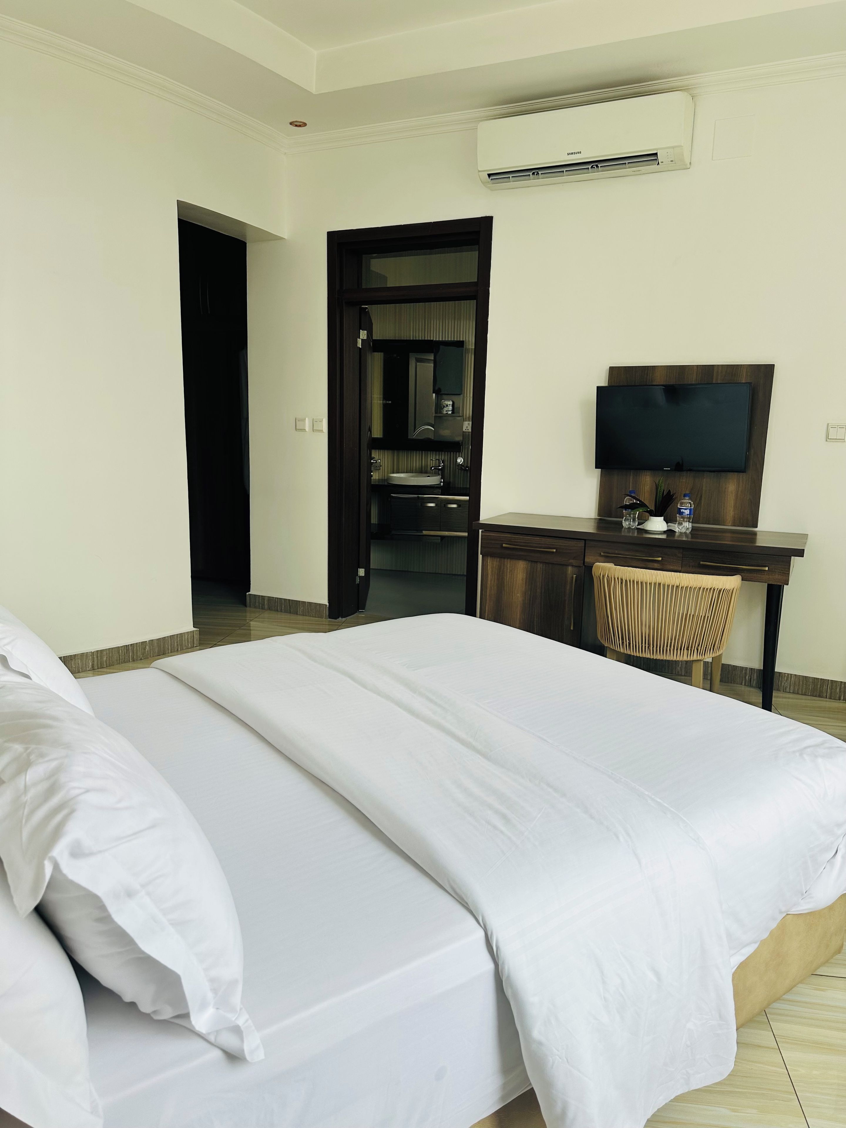 A hotel room with a bed, a desk with a chair, a television, and an air conditioning unit.