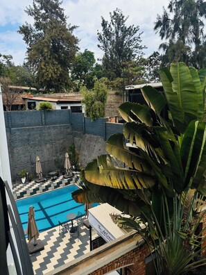 Ein Schwimmbecken mit Schachbrettmuster, umgeben von einer niedrigen Backsteinmauer und beschattet durch Sonnenschirme.