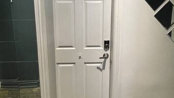 A white door with a numeric keypad lock, a vent on the floor, and a black geometric decoration on the wall.