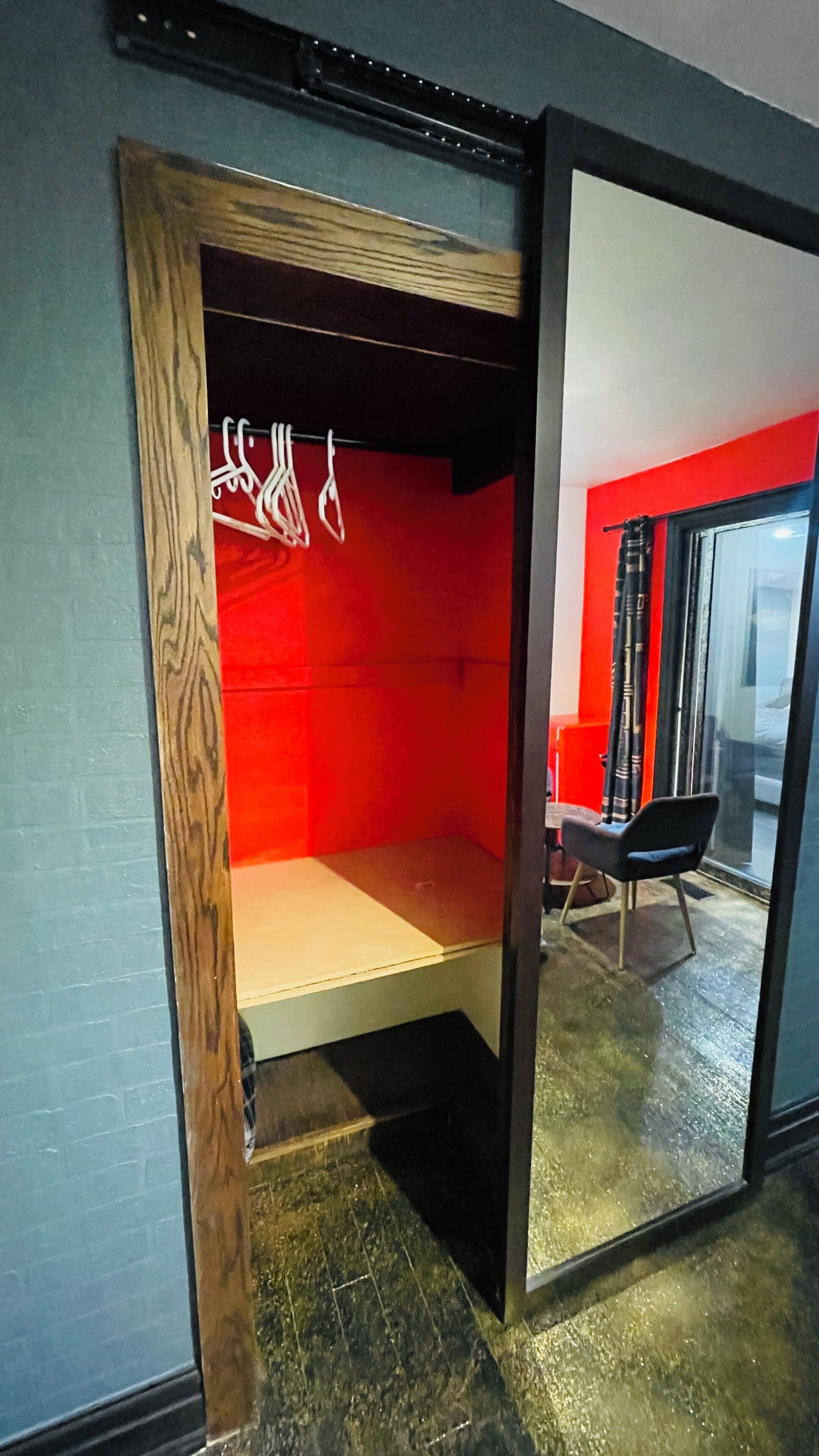 A room with a red accent wall, a wooden-framed wardrobe, and a black chair.