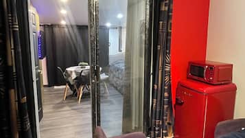 A room with a red wall, a sliding glass door leading to a dining area, a red microwave, and a small table with a remote control.