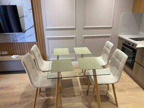 A modern kitchen with a dining table and chairs, a TV mounted on the wall, and a wooden cabinet. - Exquisite Blue Breeze - Free Parking Apartment (Sarandë)