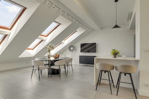 Una cocina moderna con pared de ladrillo blanco, televisor grande y comedor con mesa redonda y sillas.