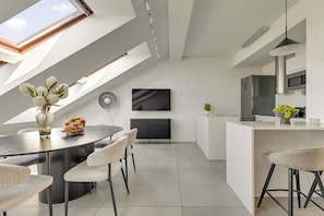 Eine moderne Küche mit Essbereich, ausgestattet mit einer weißen Ziegelwand, einem Flachbildfernseher und einer großen Kochinsel mit Mikrowelle und Backofen.