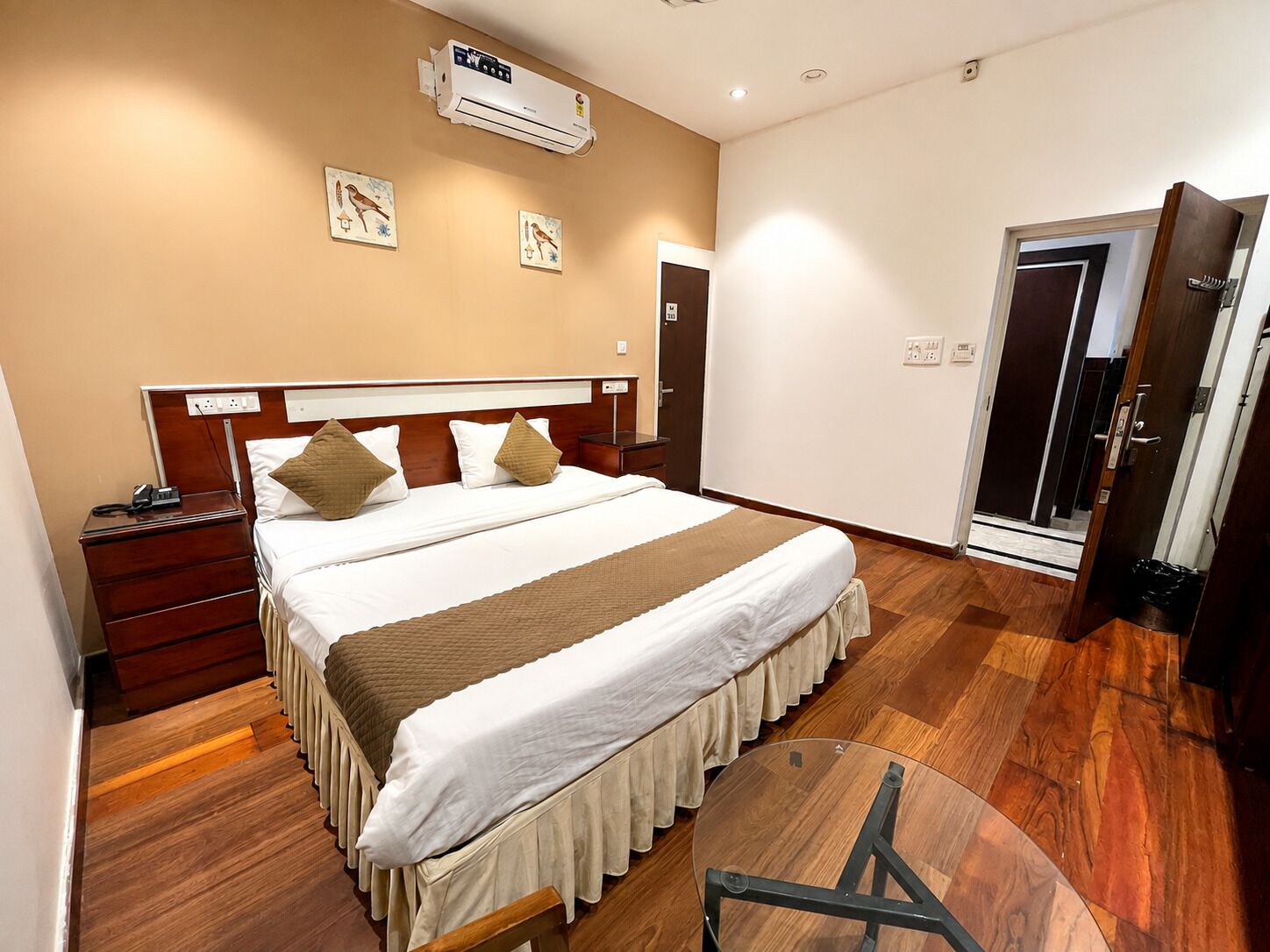 Habitació d'hotel amb llit, taula de nit, aire condicionat fixat a la paret i una porta.