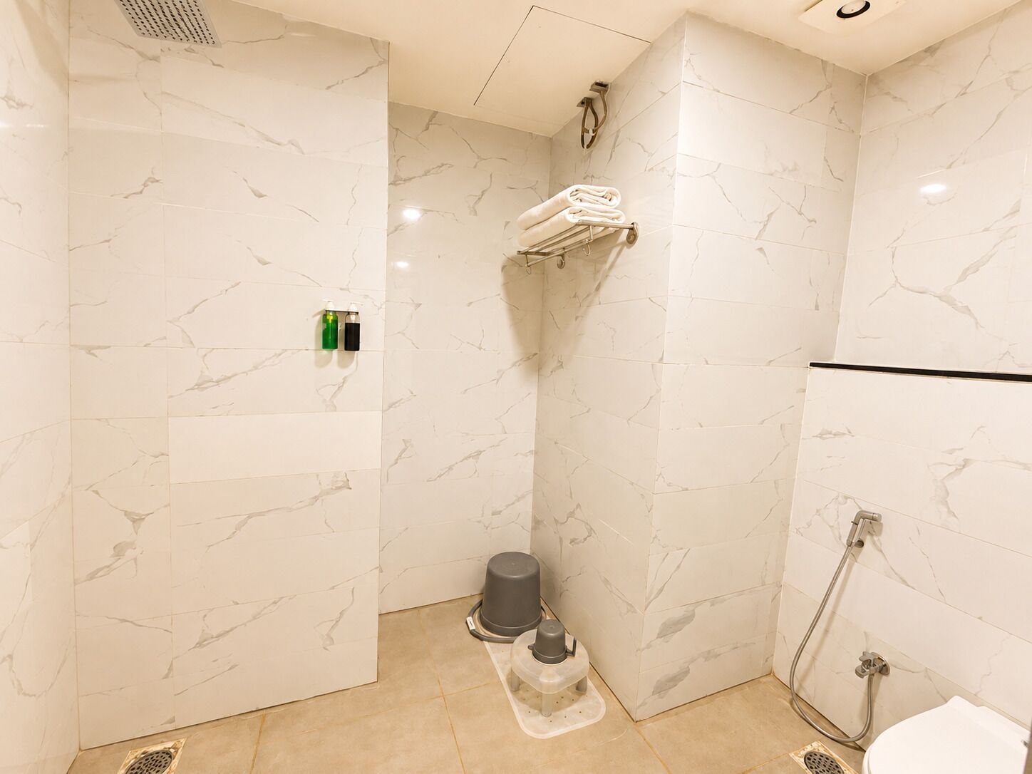 A bathroom with marble walls, a shower, a toilet, and a towel rack.