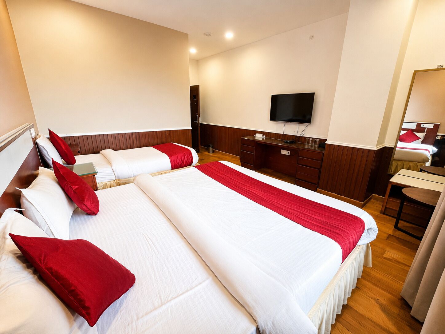 A hotel room with two beds, a desk, a television, and a mirror.